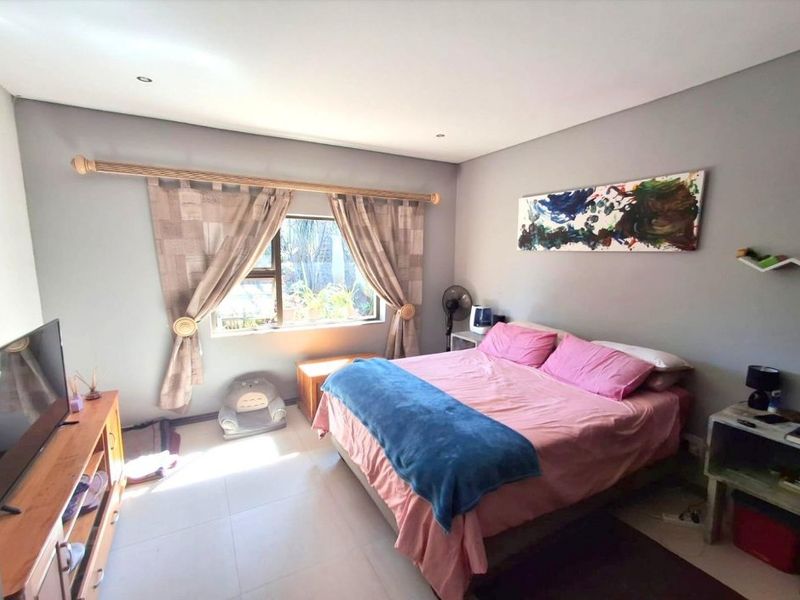 A well-lit bedroom featuring neutral grey walls, tiled flooring, and recessed downlighting, offering a comfortable and functional living space.