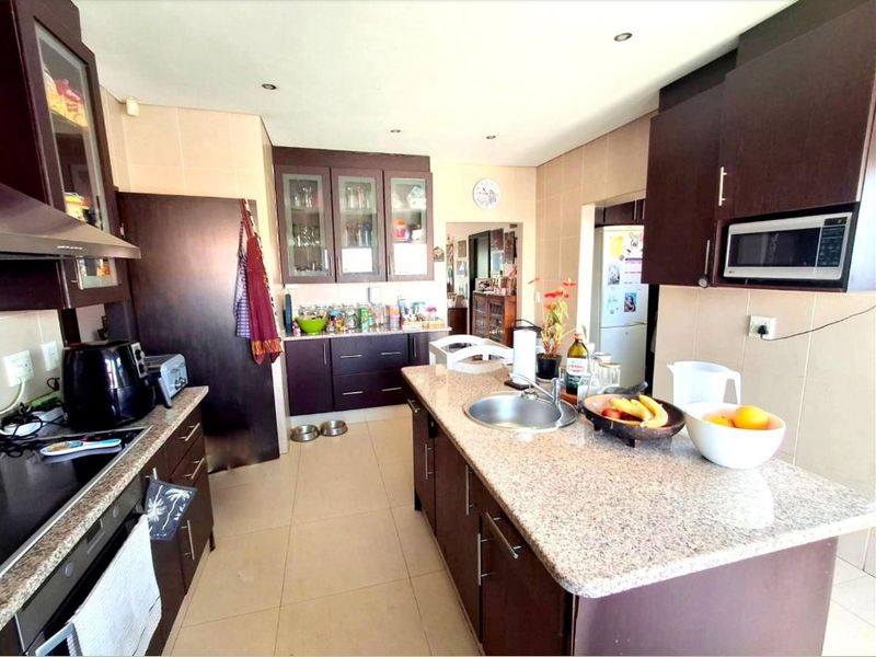 A functional kitchen featuring dark wood cabinetry, granite countertops, a central island with a sink, and integrated appliances including an oven and microwave.