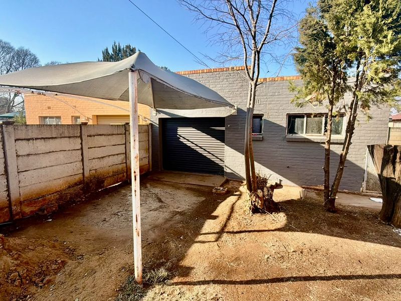 Rear exterior view featuring a brick facade, roller garage door, and a shade sail structure over an unpaved yard area.