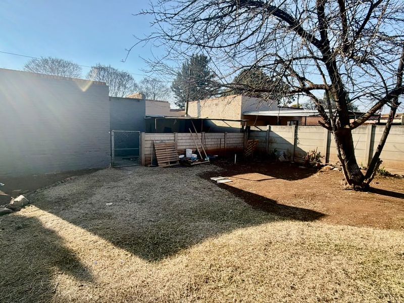 A rear garden area featuring a perimeter wall, a metal gate, and a large mature tree, with an open lawn space.