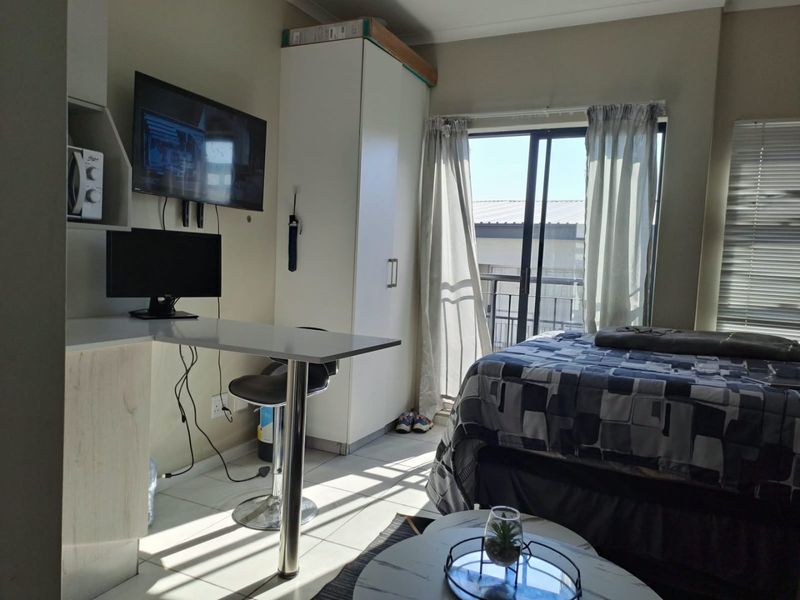 A functional bedroom featuring tiled flooring, a built-in wardrobe, a compact desk area, and a sliding glass door providing access to a balcony.