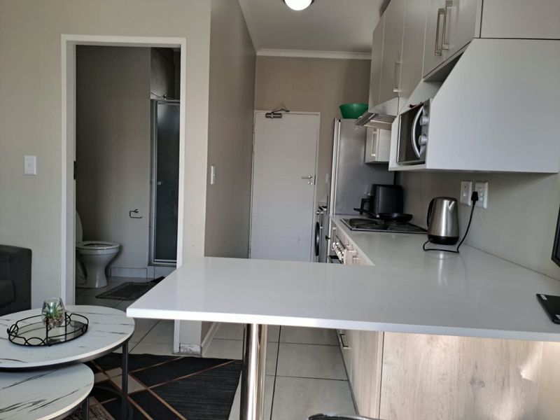 Open-plan kitchen area featuring built-in cabinetry, a breakfast counter, and tiled flooring, with an adjacent view into the bathroom.