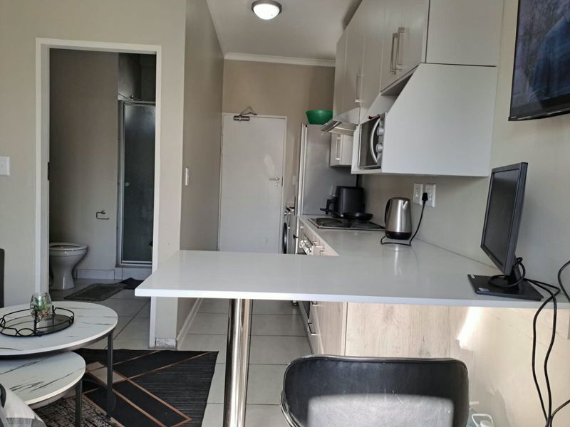 Open-plan kitchen area featuring modern white cabinetry, laminate countertops, and a breakfast bar, with direct access to the adjacent bathroom.