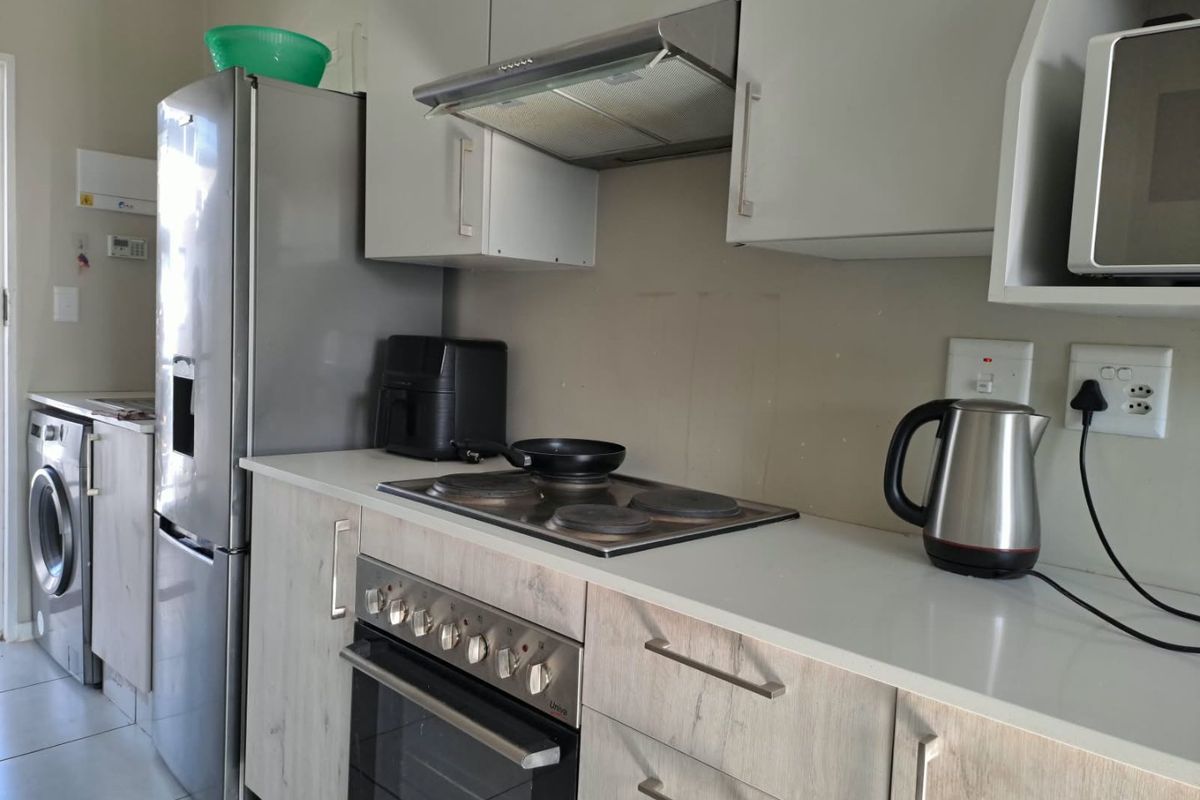A functional kitchen featuring light wood-grain cabinetry, stone countertops, a built-in electric oven with hob, and an integrated extractor fan.