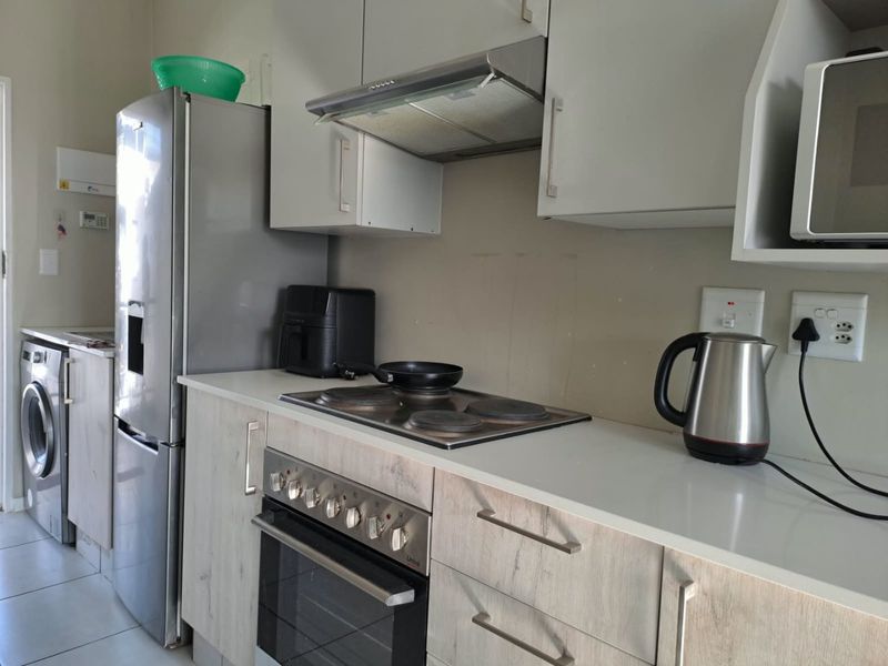 A functional kitchen featuring light wood-grain cabinetry, stone countertops, a built-in electric oven with hob, and an integrated extractor fan.