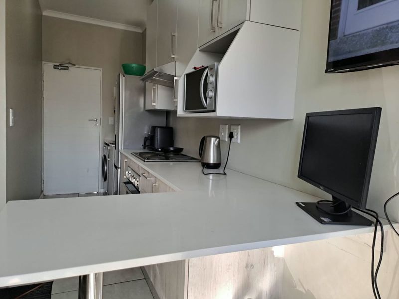 A compact, modern kitchen featuring light-toned cabinetry, stone countertops, a built-in hob, and an integrated microwave, offering a functional and efficient workspace.