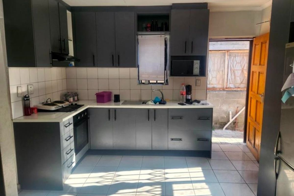 A functional kitchen featuring modern dark grey cabinetry, contrasting white countertops, tiled backsplash, and direct access to the rear exterior area.