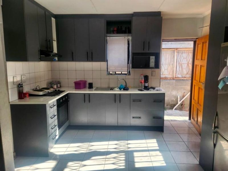 A functional kitchen featuring modern dark grey cabinetry, contrasting white countertops, tiled backsplash, and direct access to the rear exterior area.