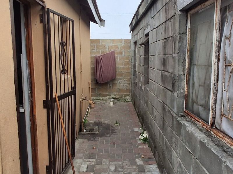 A narrow side passage between two structures featuring paved flooring, security gate access, and exposed masonry walls.
