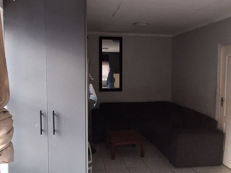 A living area featuring tiled flooring, a built-in cupboard, and ceiling lighting. The space shows signs of wear, including visible cracks in the ceiling.