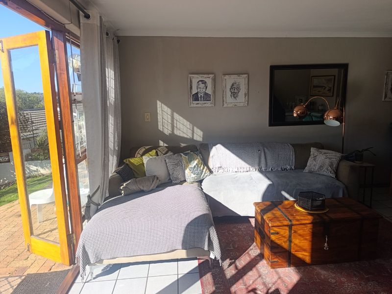 A sunlit living room featuring tiled flooring and large wooden-framed glass doors that open to an outdoor area.