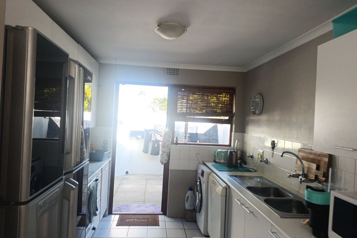 A functional kitchen featuring tiled flooring, built-in cabinetry, a double bowl stainless steel sink, and direct access to an outdoor patio area.