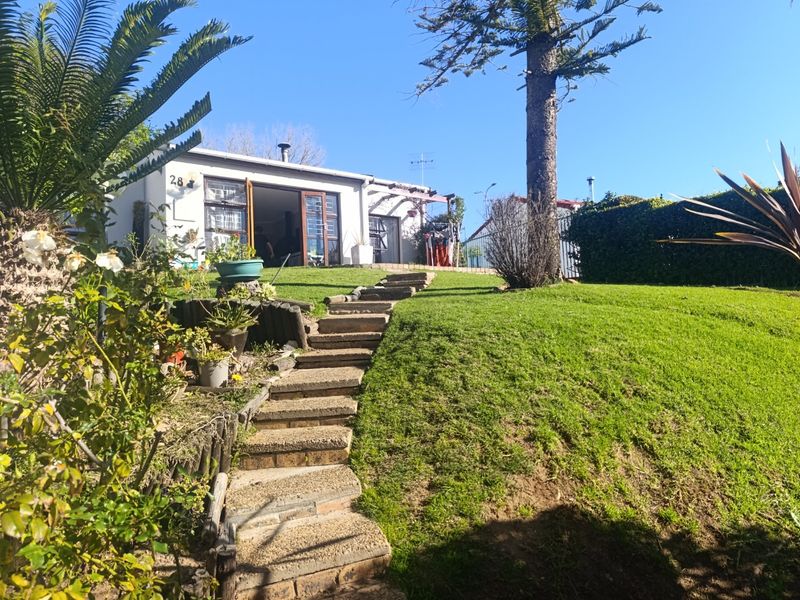 Rear view of the townhouse featuring a landscaped garden, stone staircase leading to the dwelling, and a timber pergola over the patio area.