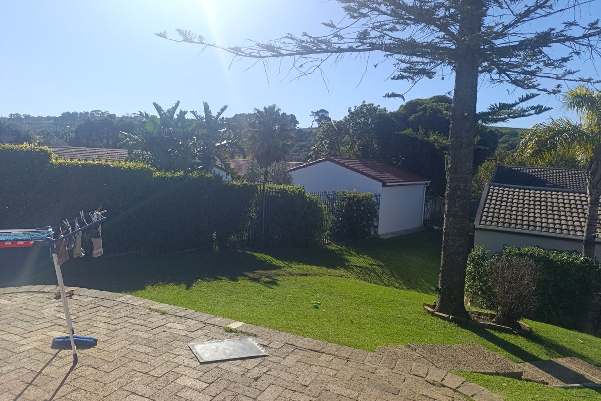 A private rear garden featuring a paved patio area, established lawn, and mature trees, providing a pleasant outdoor space for the townhouse.