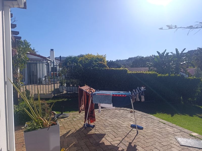 A rear garden area featuring a paved patio, established hedge boundary, and metal security gate leading to the side of the townhouse.