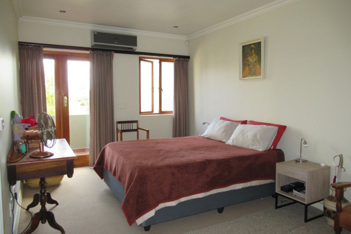 A well-maintained bedroom featuring neutral walls, carpet flooring, recessed lighting, and direct access to an outdoor balcony through a timber-framed glass door.