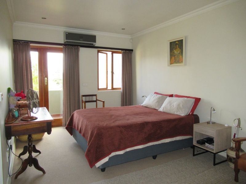 A well-maintained bedroom featuring neutral walls, carpet flooring, recessed lighting, and direct access to an outdoor balcony through a timber-framed glass door.