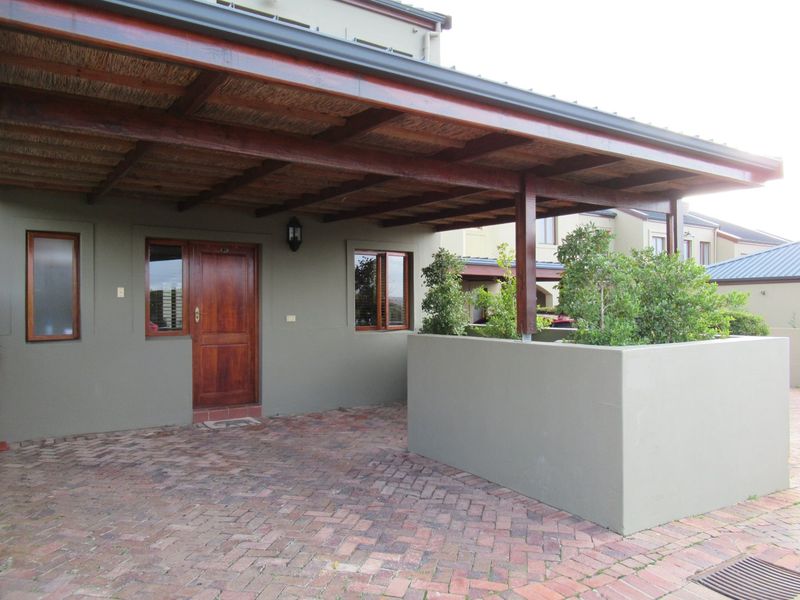 Front entrance area featuring a covered patio with a thatched roof, timber door, and brick-paved driveway with a built-in masonry planter.