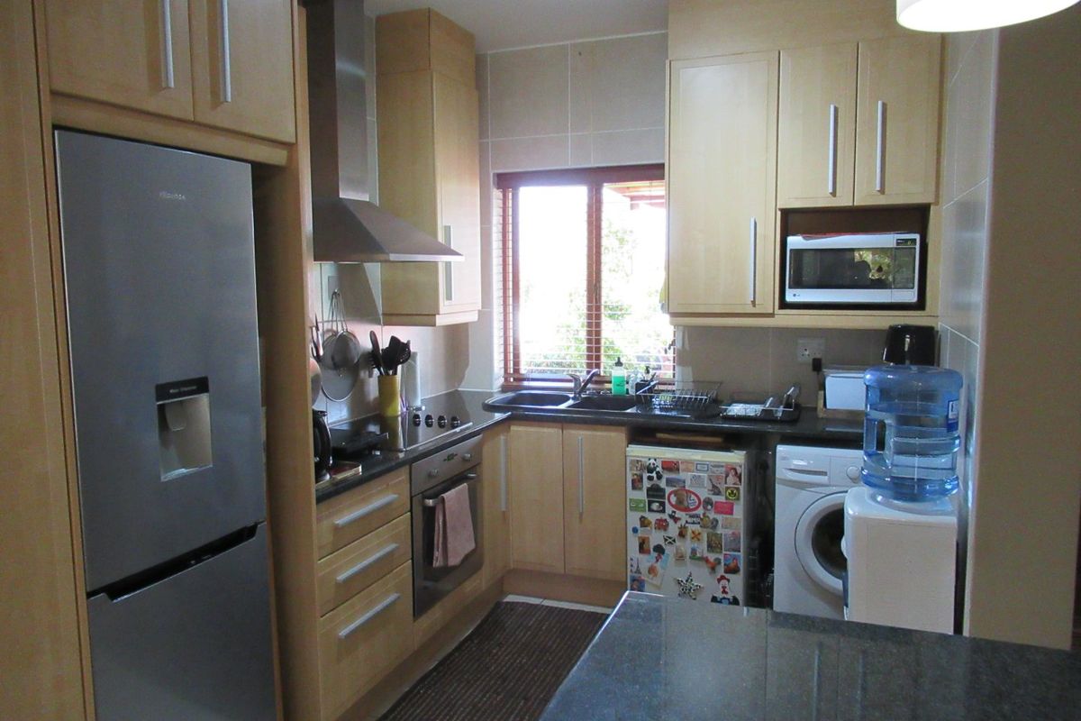 Compact kitchen featuring light wood cabinetry, granite countertops, stainless steel oven and extractor fan, and integrated laundry appliance space.