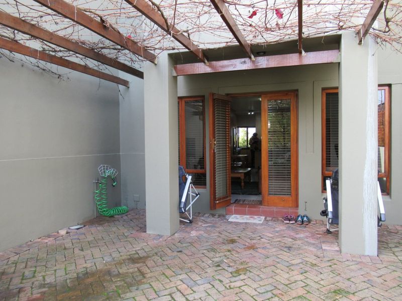 A covered patio area featuring brick paving, a timber pergola structure, and direct access to the interior through timber-framed doors.