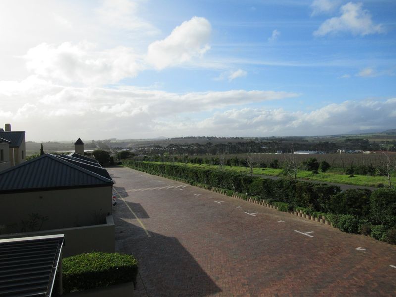 Elevated view overlooking a paved driveway, landscaped hedgerows, and expansive rural landscape under a bright sky.