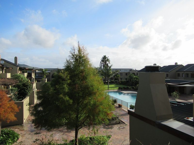 Elevated view overlooking a communal swimming pool, paved courtyard, and landscaped grounds within a residential estate complex.