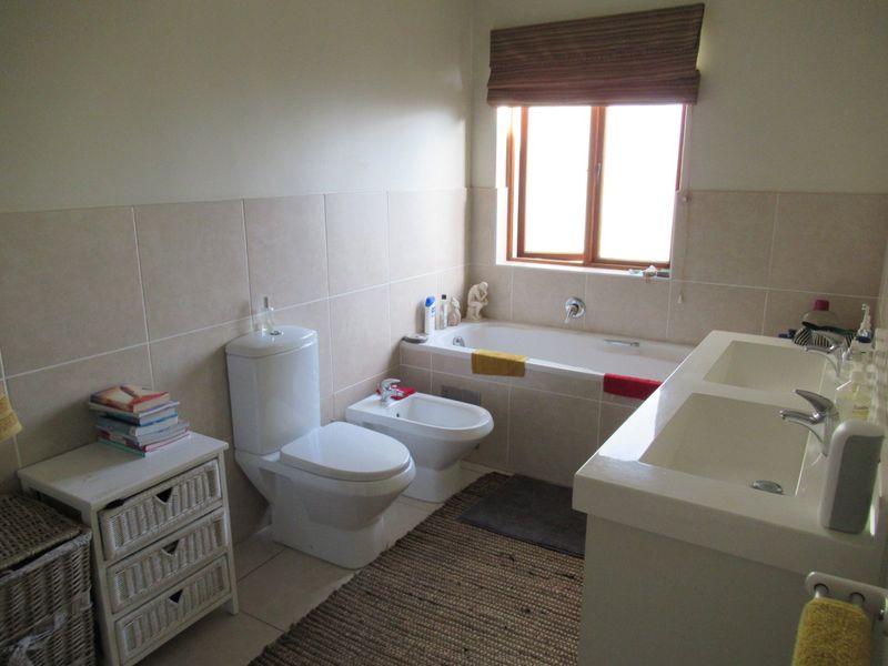A functional bathroom featuring a double vanity, built-in bathtub, bidet, and toilet with neutral wall tiling and natural light from a window.