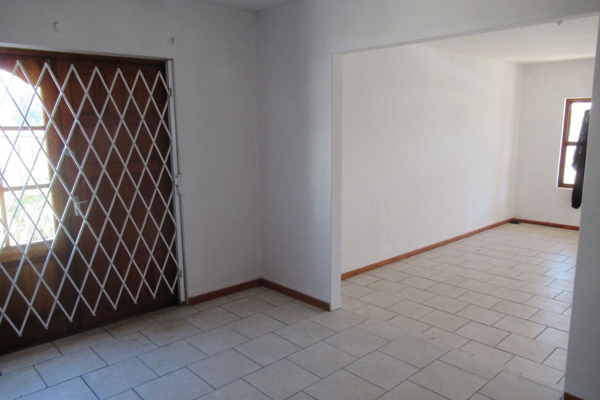 An empty, open-plan living area featuring neutral tiled flooring, white walls, and a secure timber entrance door with a metal security gate.