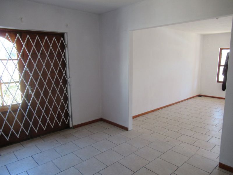 An empty, open-plan living area featuring neutral tiled flooring, white walls, and a secure timber entrance door with a metal security gate.