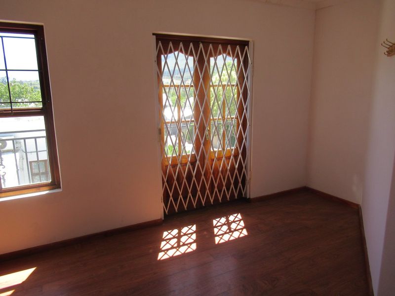 An empty bedroom featuring laminate flooring, timber-framed windows, and double doors with a security gate, offering natural light and a neutral interior.