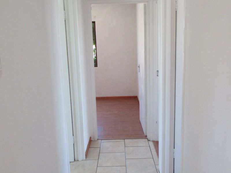 A clean, empty hallway featuring tiled flooring transitioning into laminate flooring, connecting multiple rooms within the home.