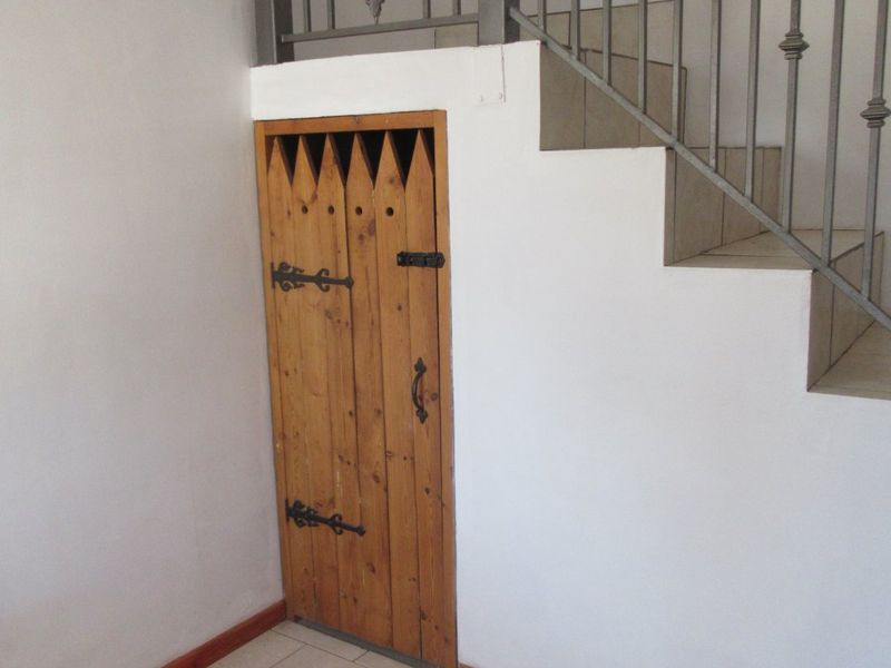 A hallway area featuring a staircase with a wrought iron balustrade and a built-in under-stair storage cupboard with a wooden door.