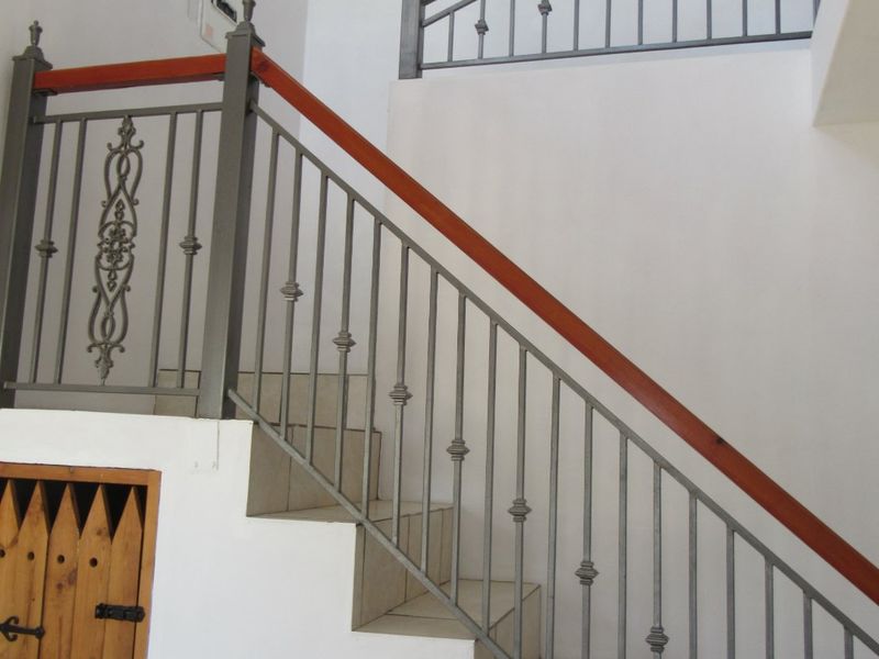 A bright hallway featuring a tiled staircase with a decorative wrought iron balustrade, wooden handrail, and convenient under-stair storage access.