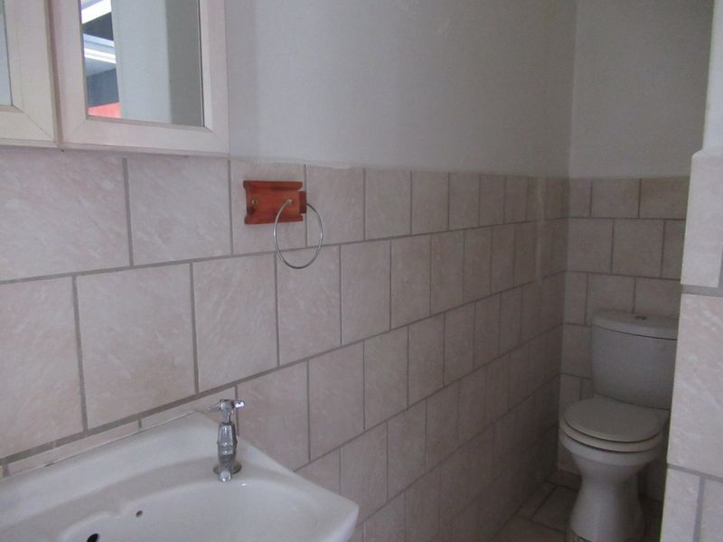 A functional bathroom featuring neutral wall tiles, a pedestal basin, and a standard toilet, offering a clean and simple layout.
