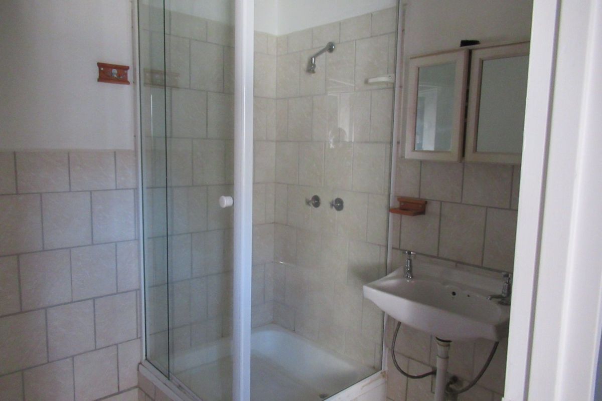 A functional bathroom featuring a glass shower enclosure, wall-mounted basin, and neutral wall tiling.