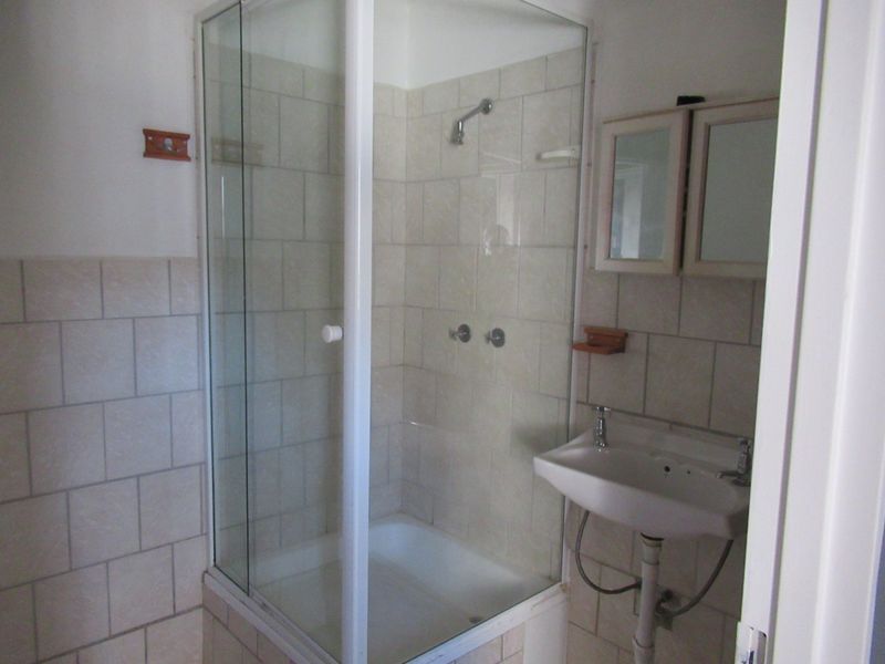 A functional bathroom featuring a glass shower enclosure, wall-mounted basin, and neutral wall tiling.