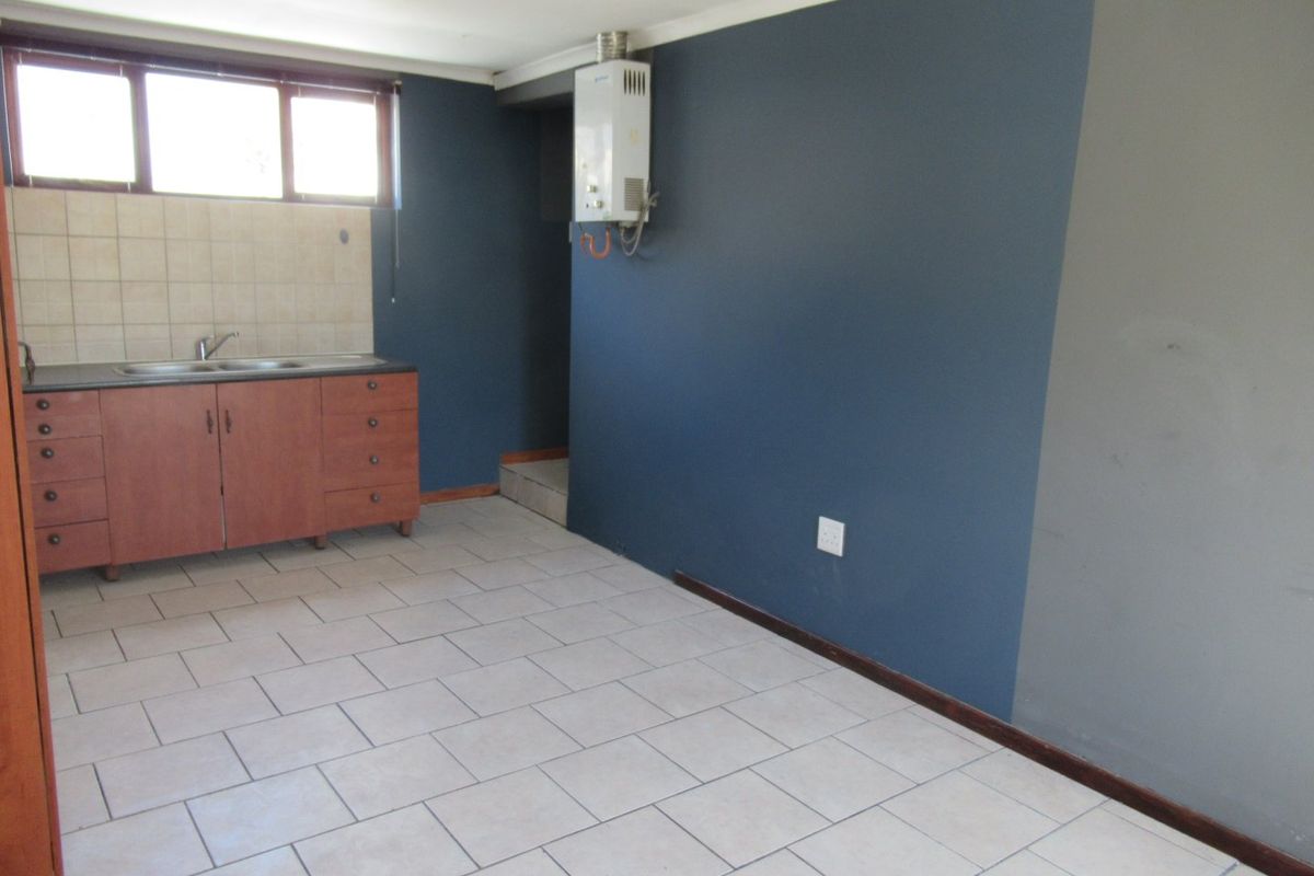 A compact, empty kitchen area featuring tiled flooring, built-in cabinetry with a stainless steel sink, and a wall-mounted gas geyser.