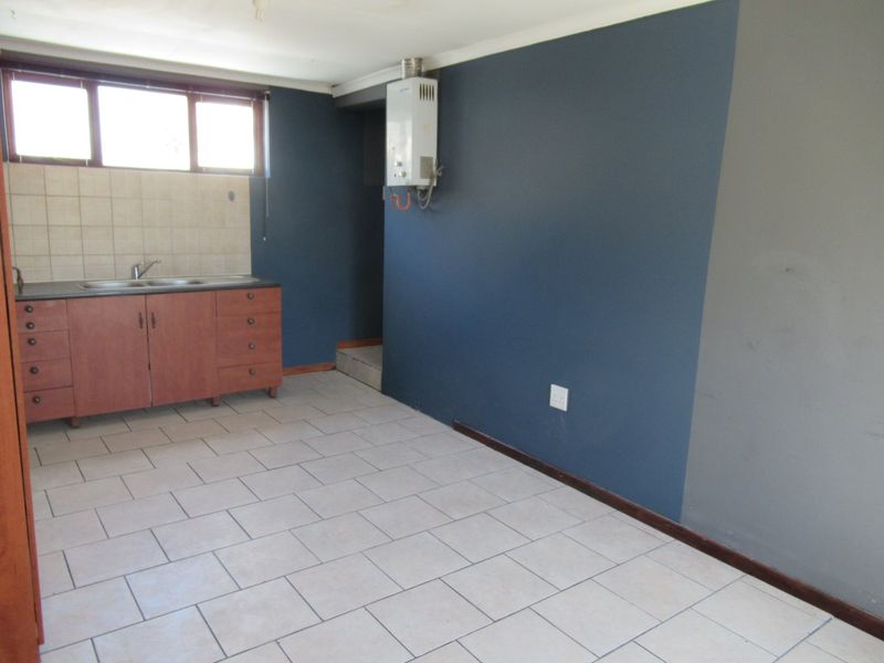 A compact, empty kitchen area featuring tiled flooring, built-in cabinetry with a stainless steel sink, and a wall-mounted gas geyser.