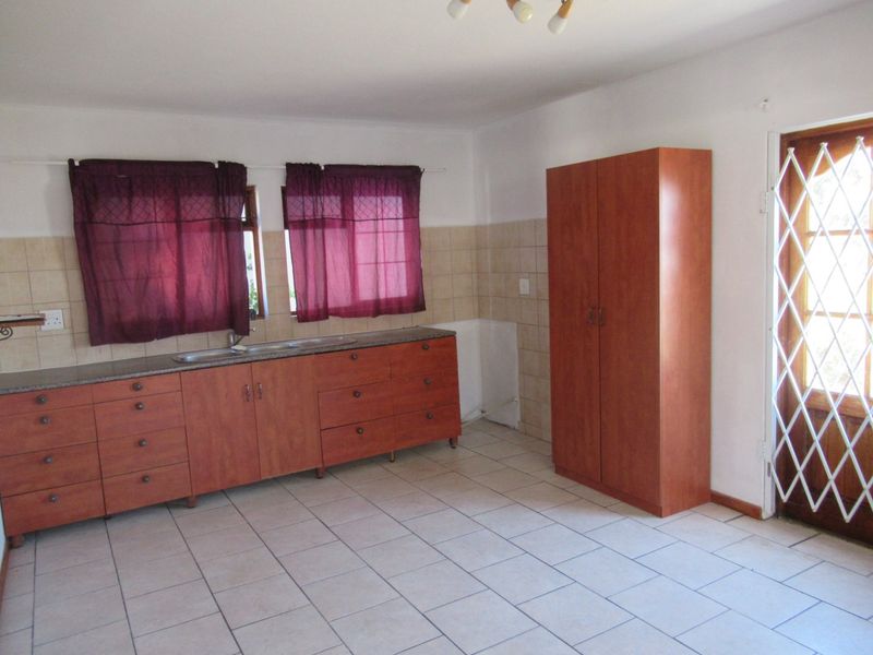 Kitchen featuring built-in wooden cabinetry, granite countertops, double sink, and tiled flooring with direct access to the exterior via a security gate.