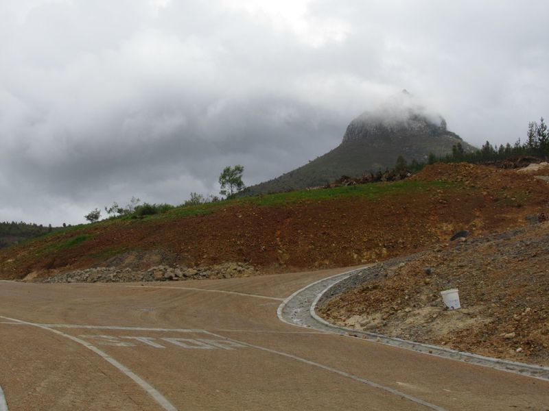 A view of a paved residential road with concrete curbing and drainage, set against a backdrop of undeveloped land and a mountain.