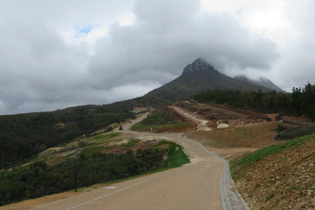 A view of a paved access road winding through a residential development with mountain views and established perimeter fencing.