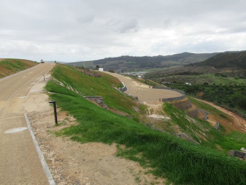 An elevated view of a residential development site featuring paved roads, landscaped embankments, and stone retaining walls overlooking a valley.