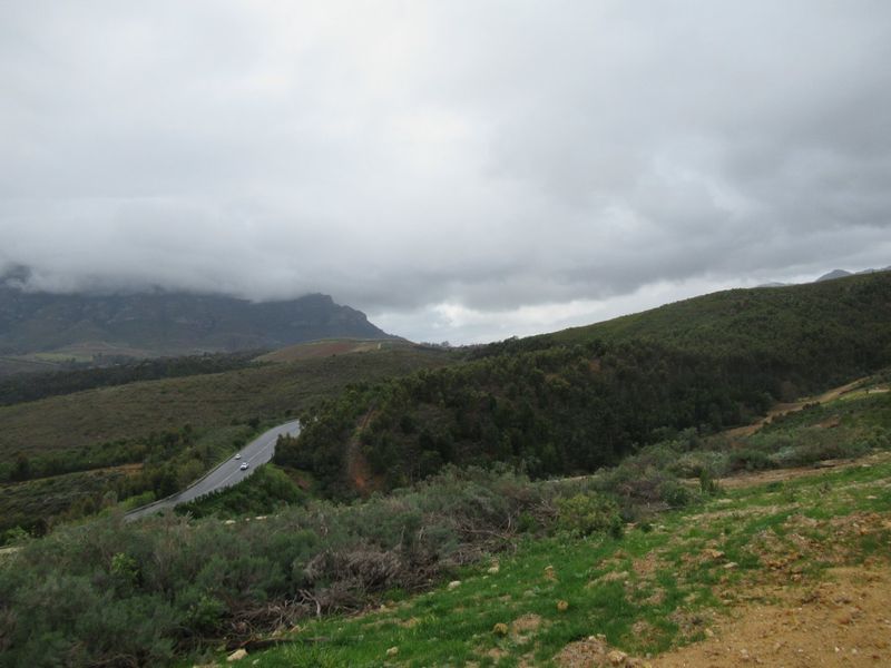 A scenic view of the surrounding natural landscape, featuring rolling hills, native vegetation, and a distant mountain range under a cloudy sky.