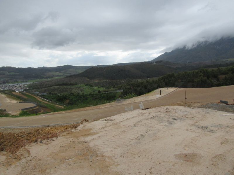 A wide-angle view of a vacant residential plot featuring graded earth and expansive mountain landscape views.