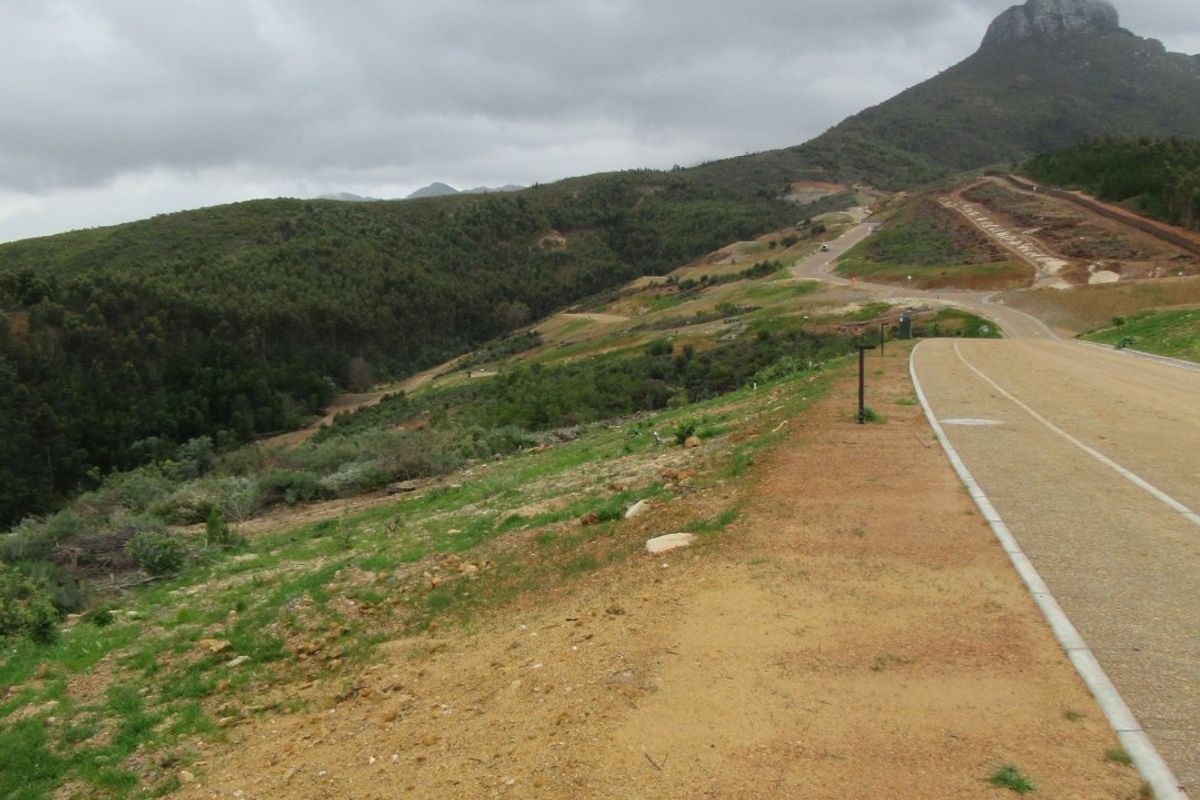 A view of a paved road winding through a natural landscape with mountain views in the background.