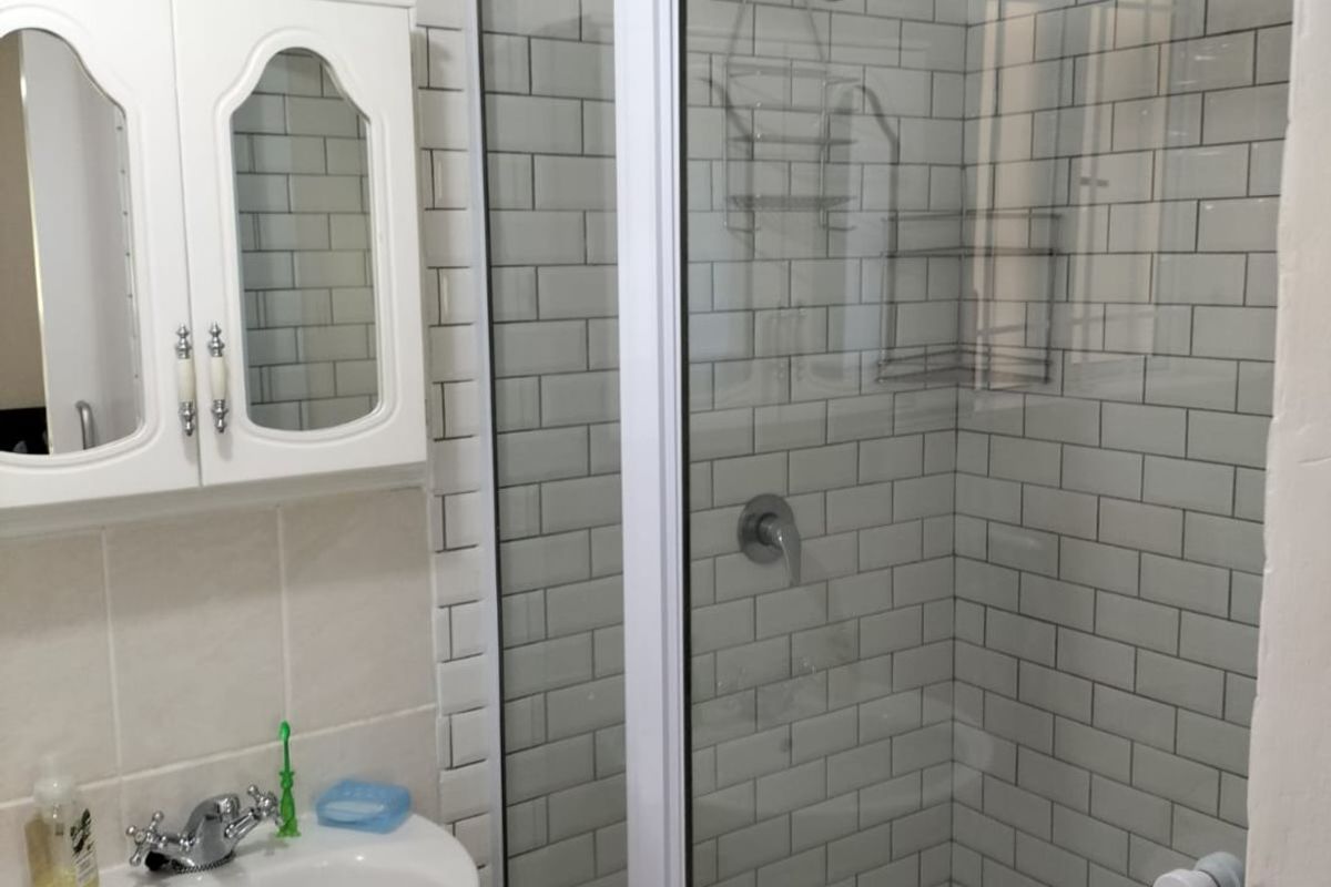 A clean bathroom featuring a pedestal basin, a glass-enclosed shower with subway tile surround, and a wall-mounted medicine cabinet.