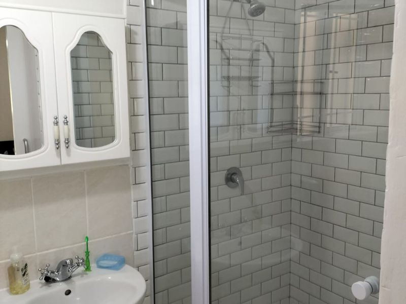 A clean bathroom featuring a pedestal basin, a glass-enclosed shower with subway tile surround, and a wall-mounted medicine cabinet.