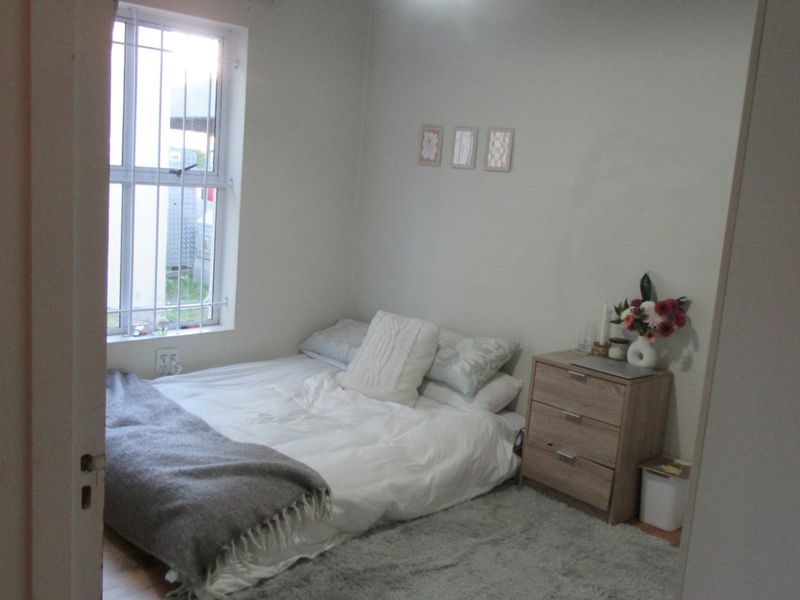 A compact bedroom featuring laminate flooring, a window with security bars, and a central pendant light fixture.