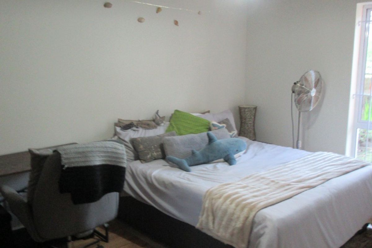 A functional bedroom featuring laminate flooring, a central pendant light, and a sliding glass door providing natural light.