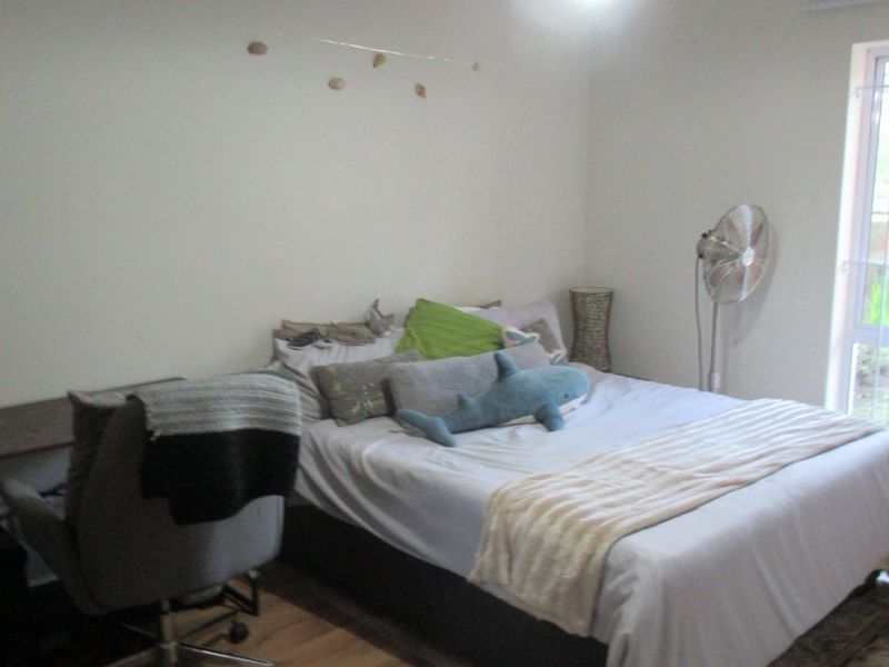 A functional bedroom featuring laminate flooring, a central pendant light, and a sliding glass door providing natural light.
